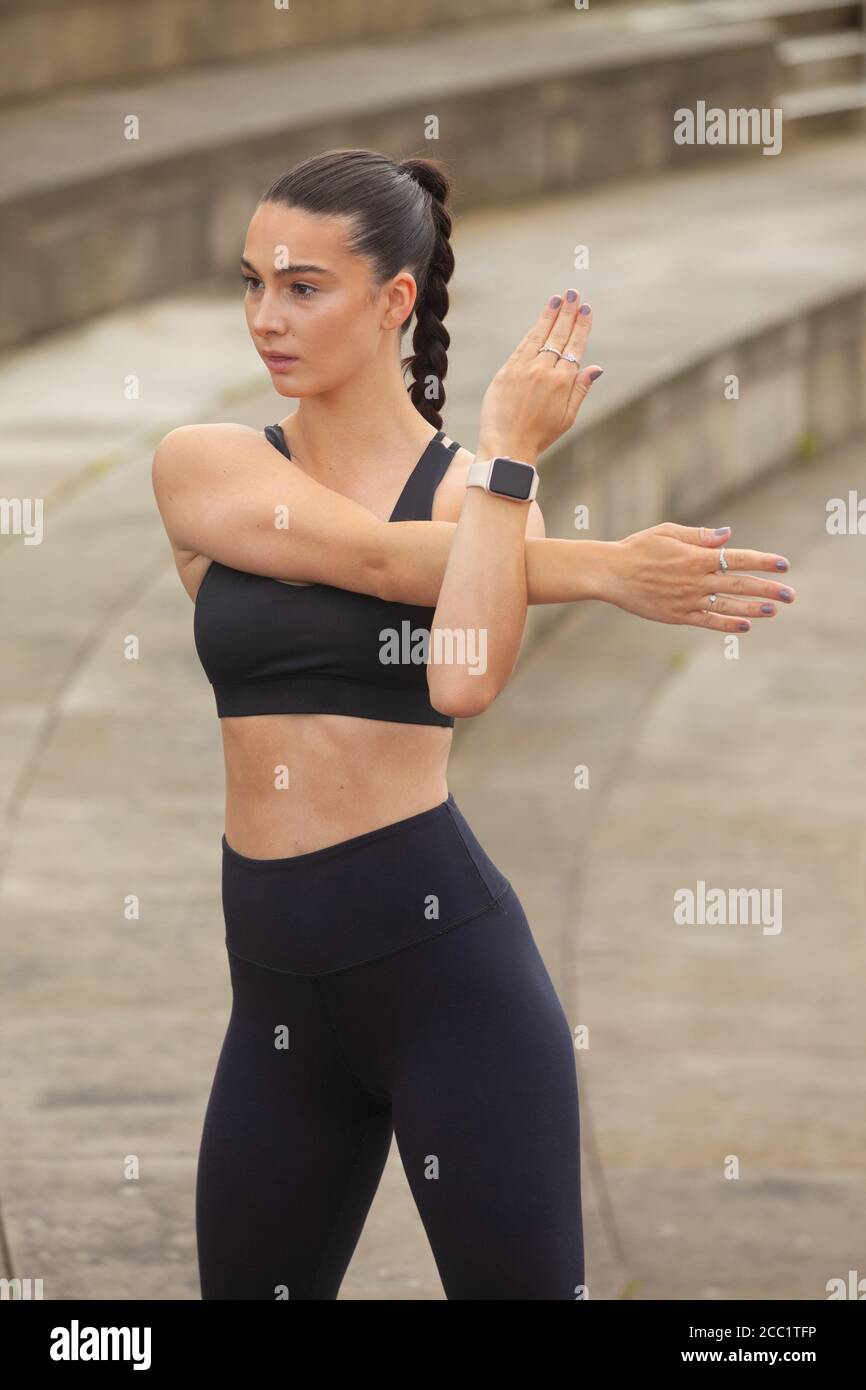 Woman wearing leggings and sports bra doing an arm stretch Stock Photo