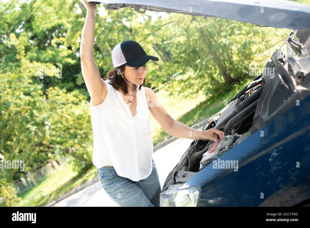 A woman waits for assistance near her car broken down on the road side. Stock Photo