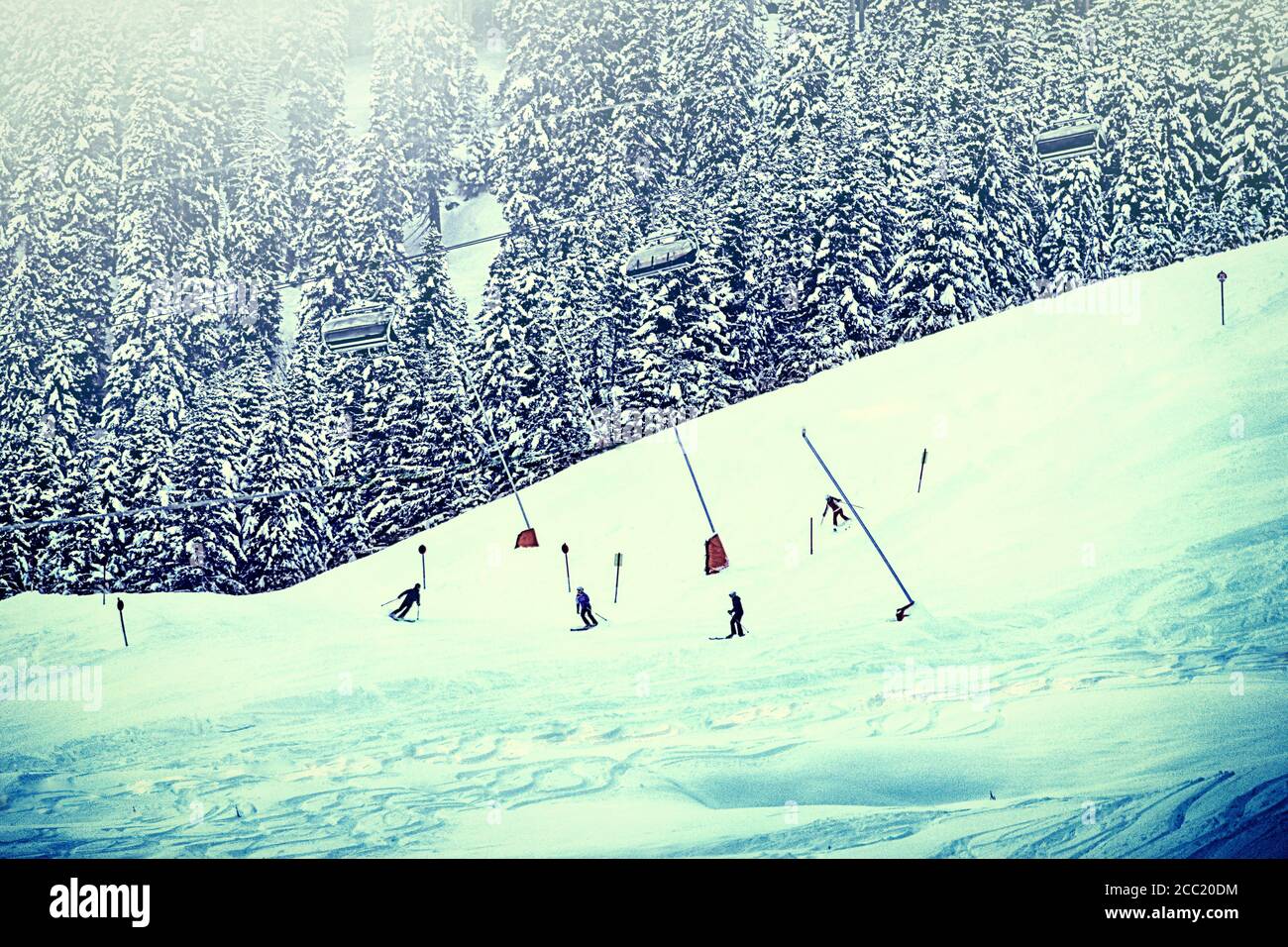 Austria - Skiers on a sky slope bordered by fir trees on the Tauern Alps,with cable cars passing over Stock Photo
