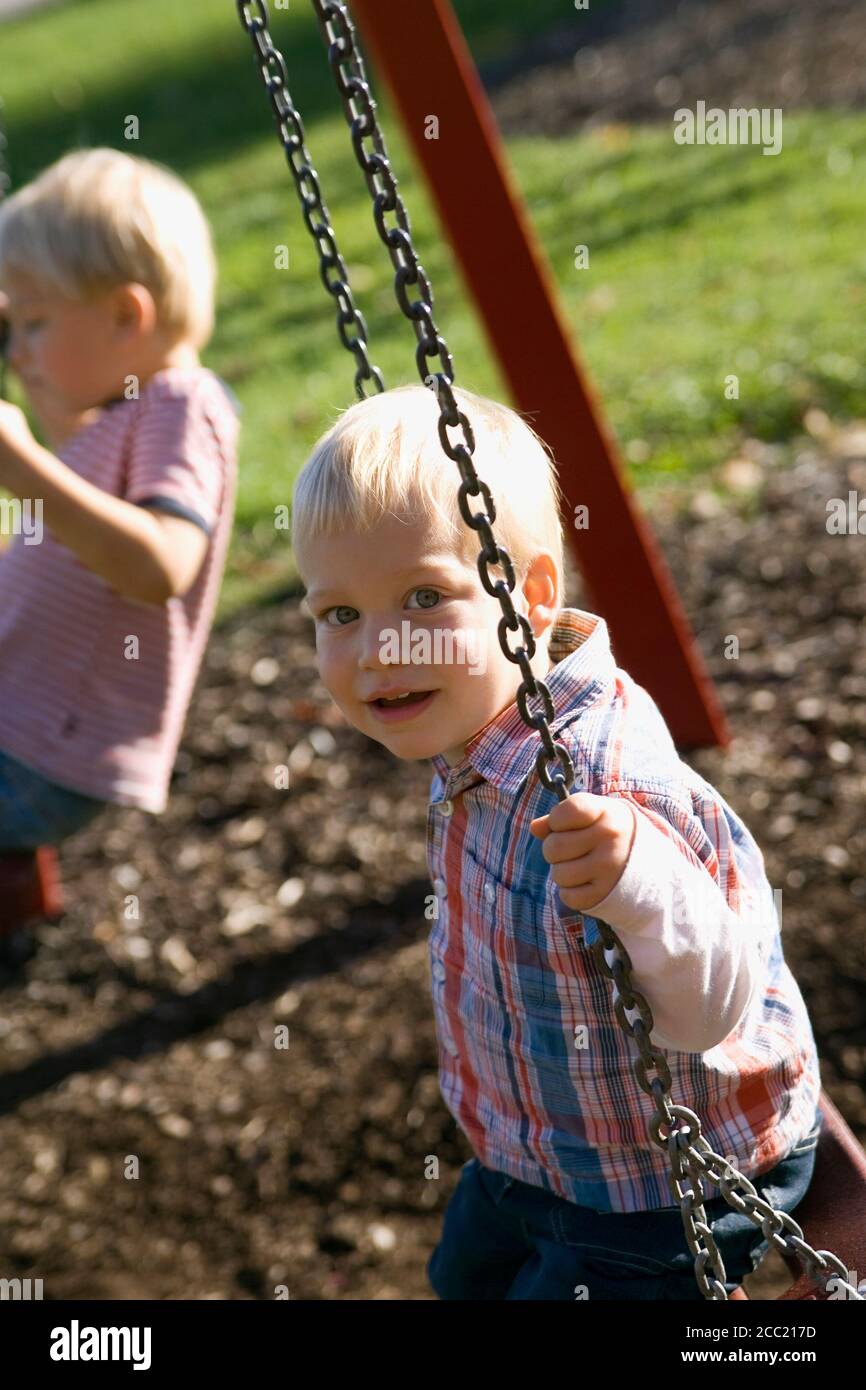 Two little boys ( 2-3) (4-5) sitting on swing Stock Photo