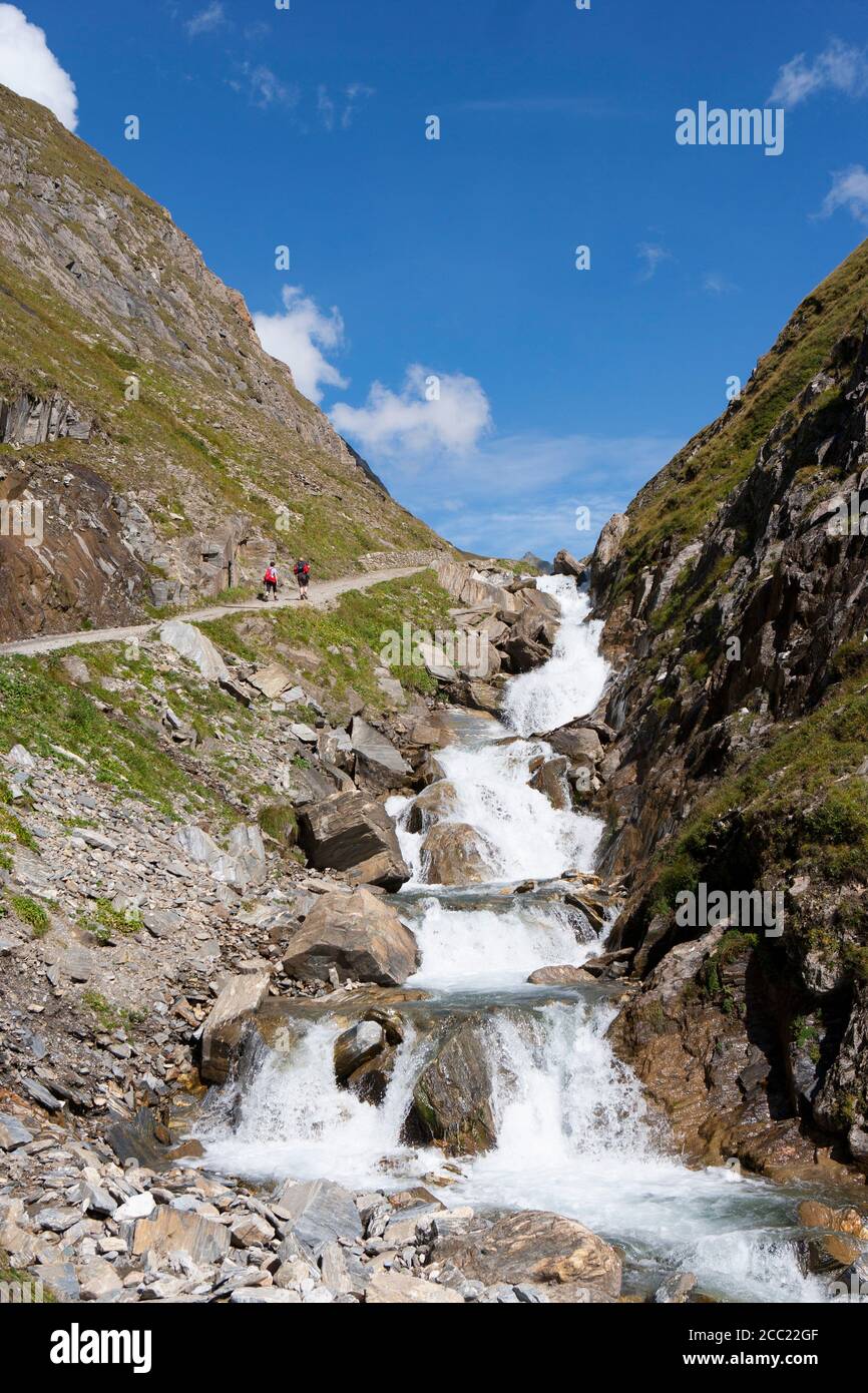 Italy, View of Pfunderer Berge with hikers walking near stream Stock Photo