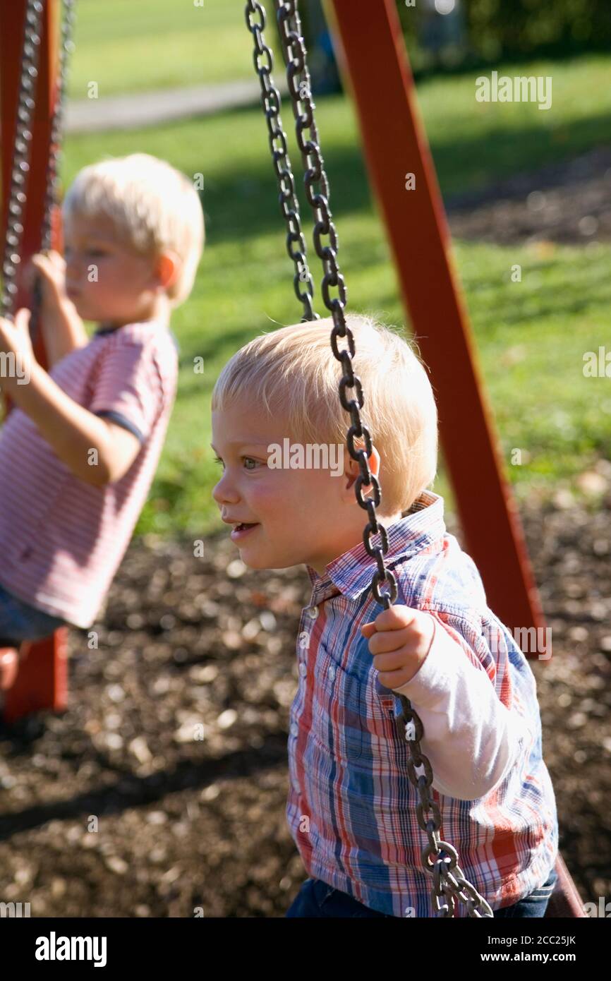 Two little boys ( 2-3) (4-5) sitting on swing Stock Photo