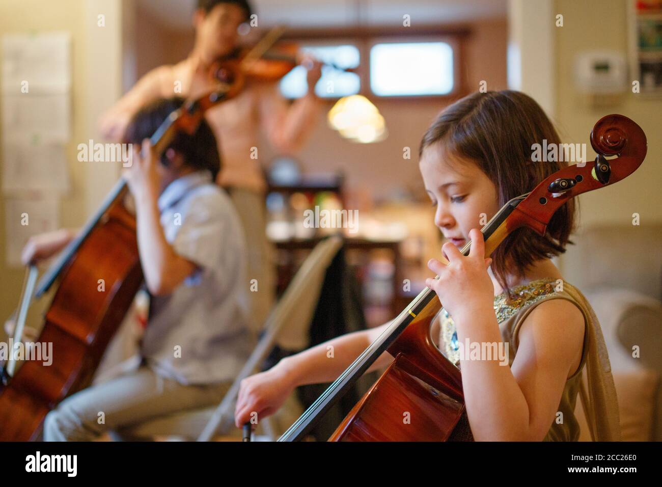 A small child plays cello concert with her family in the living room Stock Photo