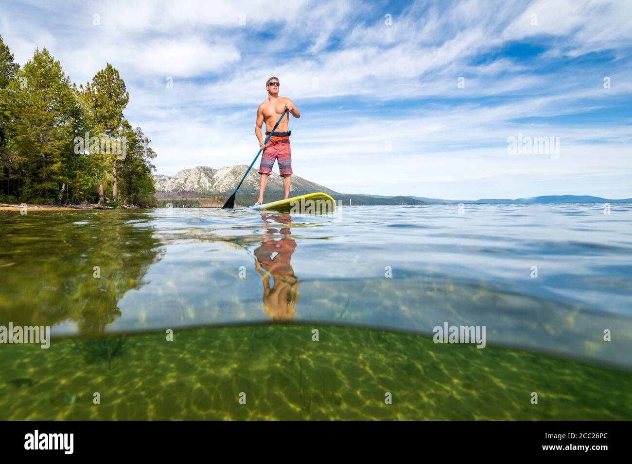 An over-under shot of a man stand-up paddleboarding on a summer day in South Lake Tahoe, California. Stock Photo