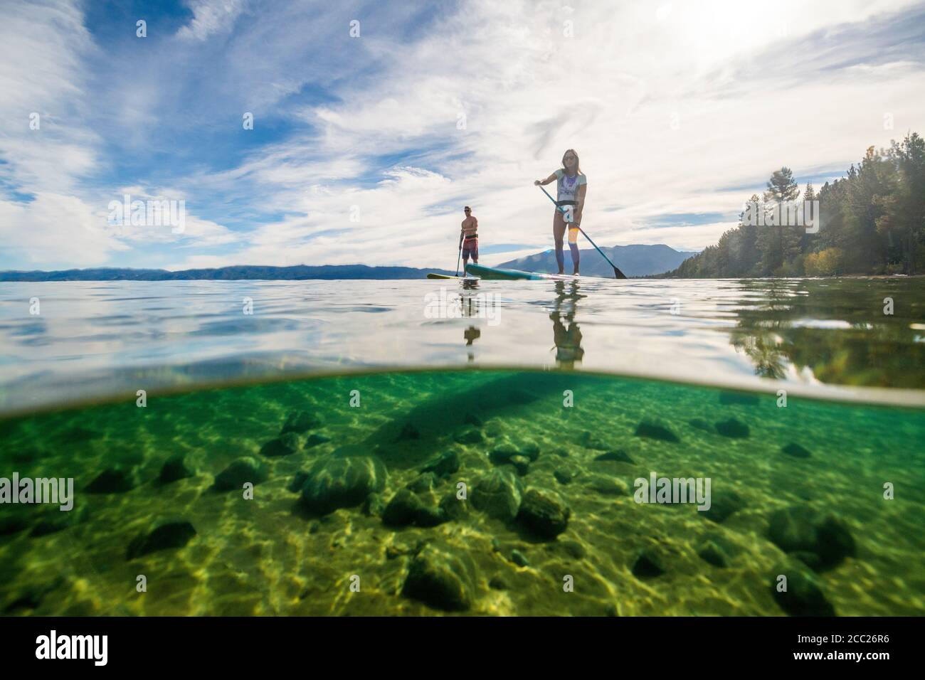 An over-under shot of two paddle-boarders enjoying a summer morning exploring the beautiful, clear waters of South Lake Tahoe, California. Stock Photo