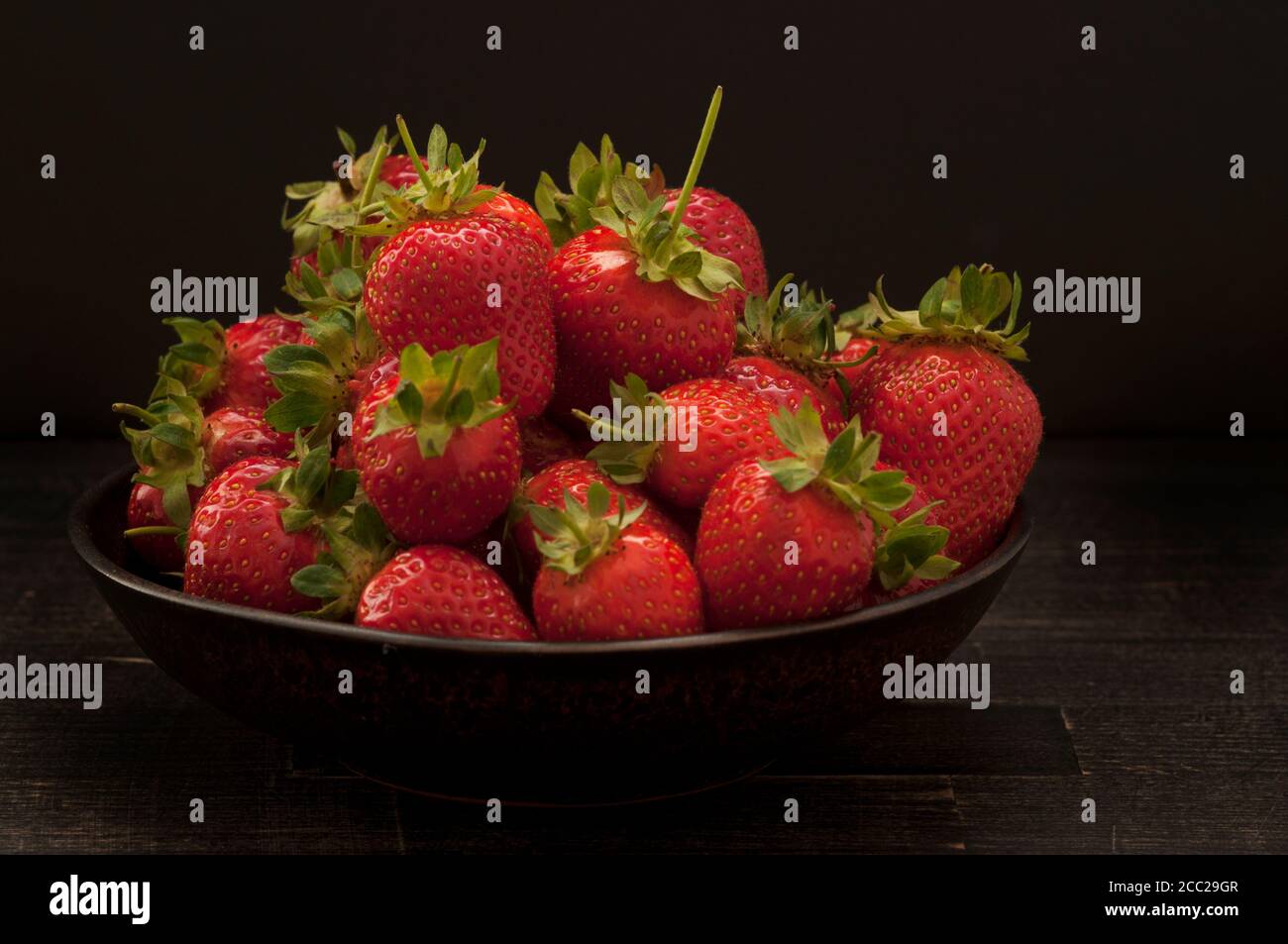 Bowl of strawberries on wooden table, close up Stock Photo