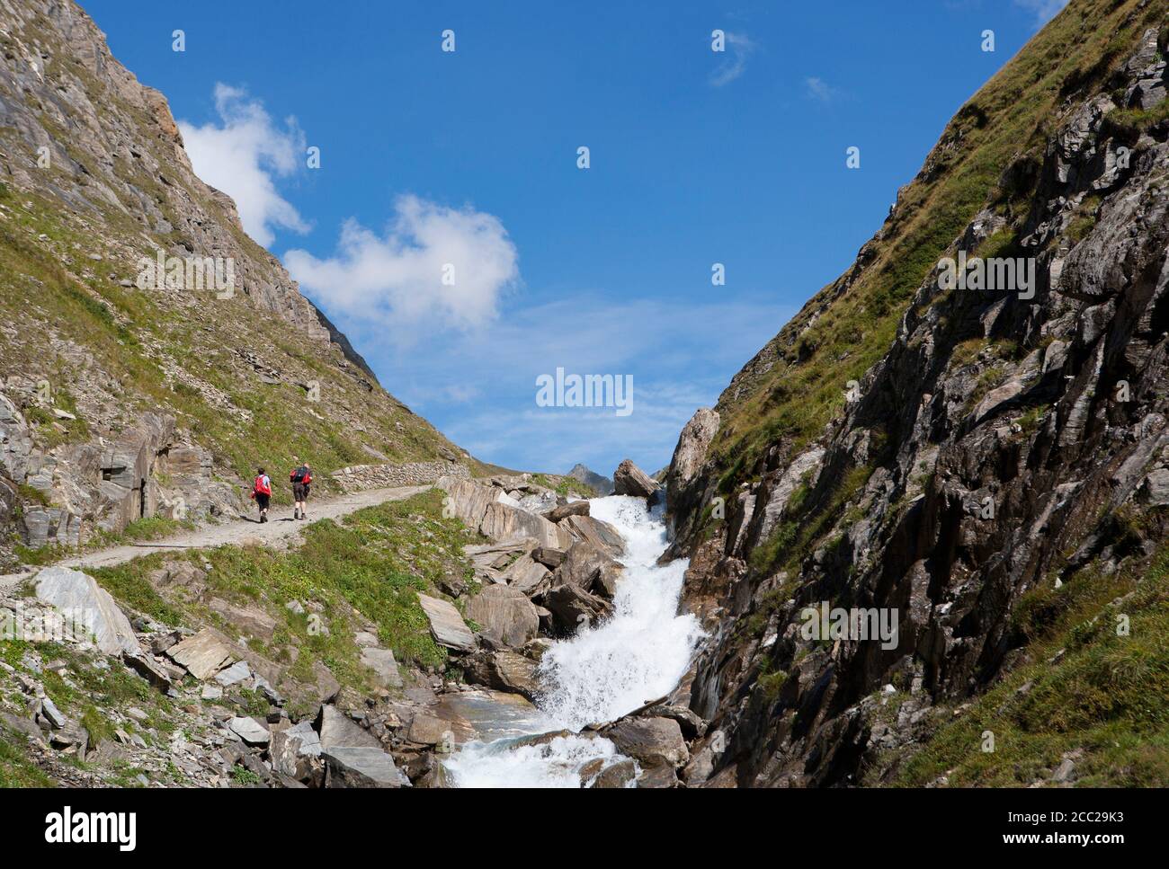 Italy, View of Pfunderer Berge with hikers walking near stream Stock Photo
