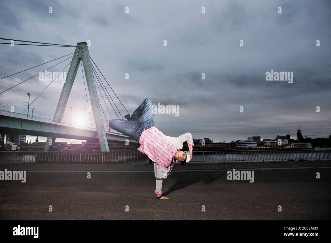 Germany, Cologne, Young man performing breakdance, Rhine bridge in background Stock Photo