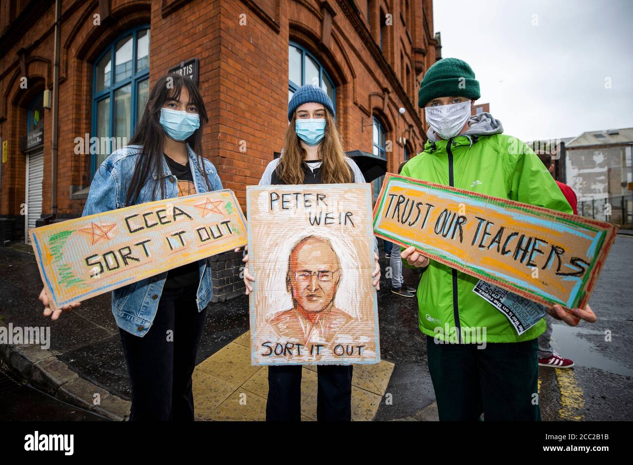(left to right) Kylie McComb and Kathleen Malone, GSCE students from Belfast Royal Academy, with Ruben Hughes from St Malachy's College Belfast, show their homemade signs during a protest at the Northern Ireland Education Authority main building in Belfast, over Northern Ireland Minister of Education, Peter Weir's decision on A-level results. Stock Photo