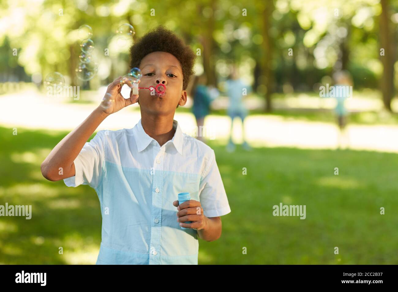 Waist up portrait of teenage African-American boy blowing bubbles while standing in green park outdoors, copy space Stock Photo