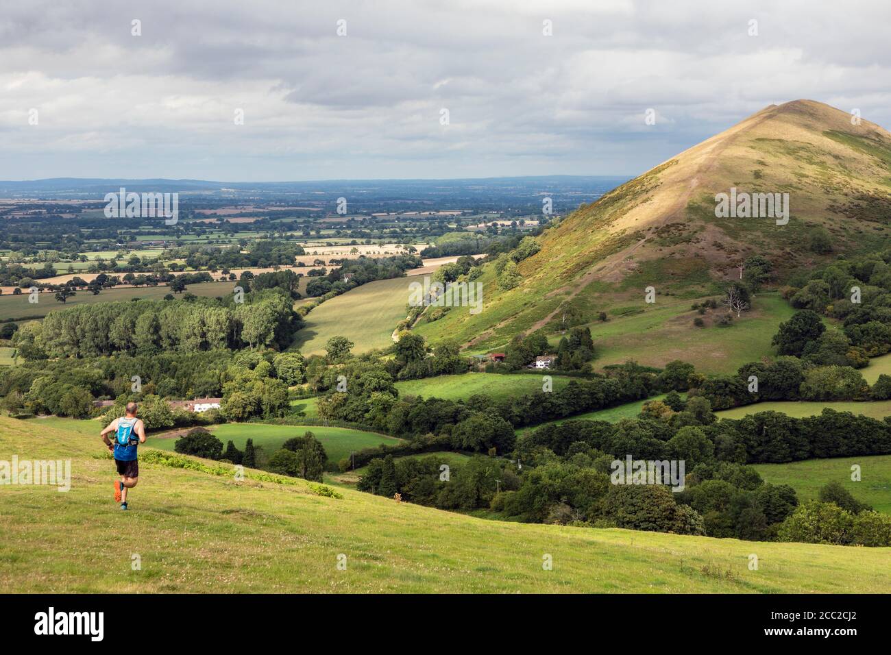 Jogger running down Little Caradoc towards the hamlet of Comley and looking towards The Lawley, Shropshire Hills near Church Stretton Stock Photo