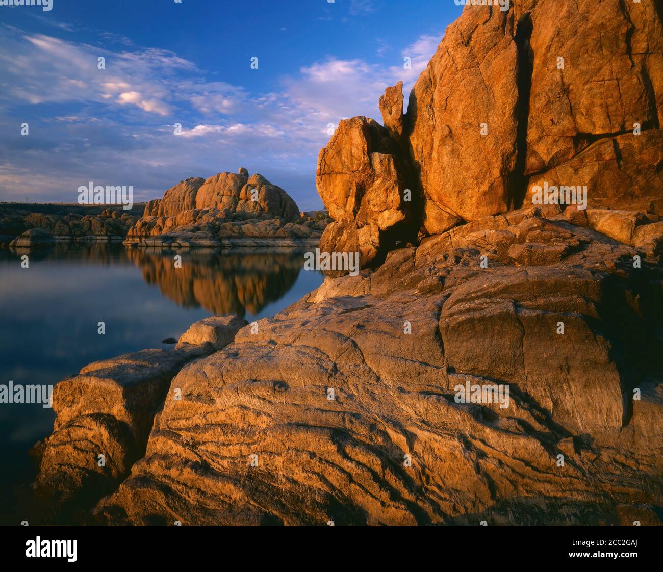 Prescott  Yavapai County  AZ / First light on the textured granite shoreline with an island of boulders beyond on a placid Watson Lake in the Prescott Stock Photo