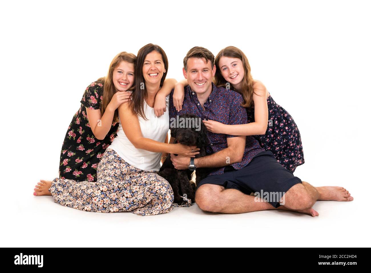Horizontal portrait of a young family with their dog against a white background in a studio or high key. Stock Photo