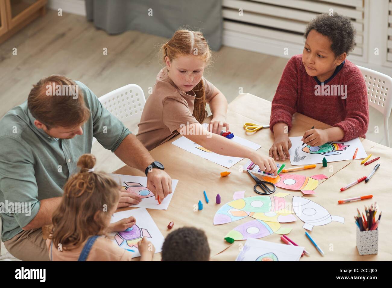 High angle view at multi-ethnic group of kids drawing pictures with crayons while enjoying art and craft class in pre school or development center, co Stock Photo