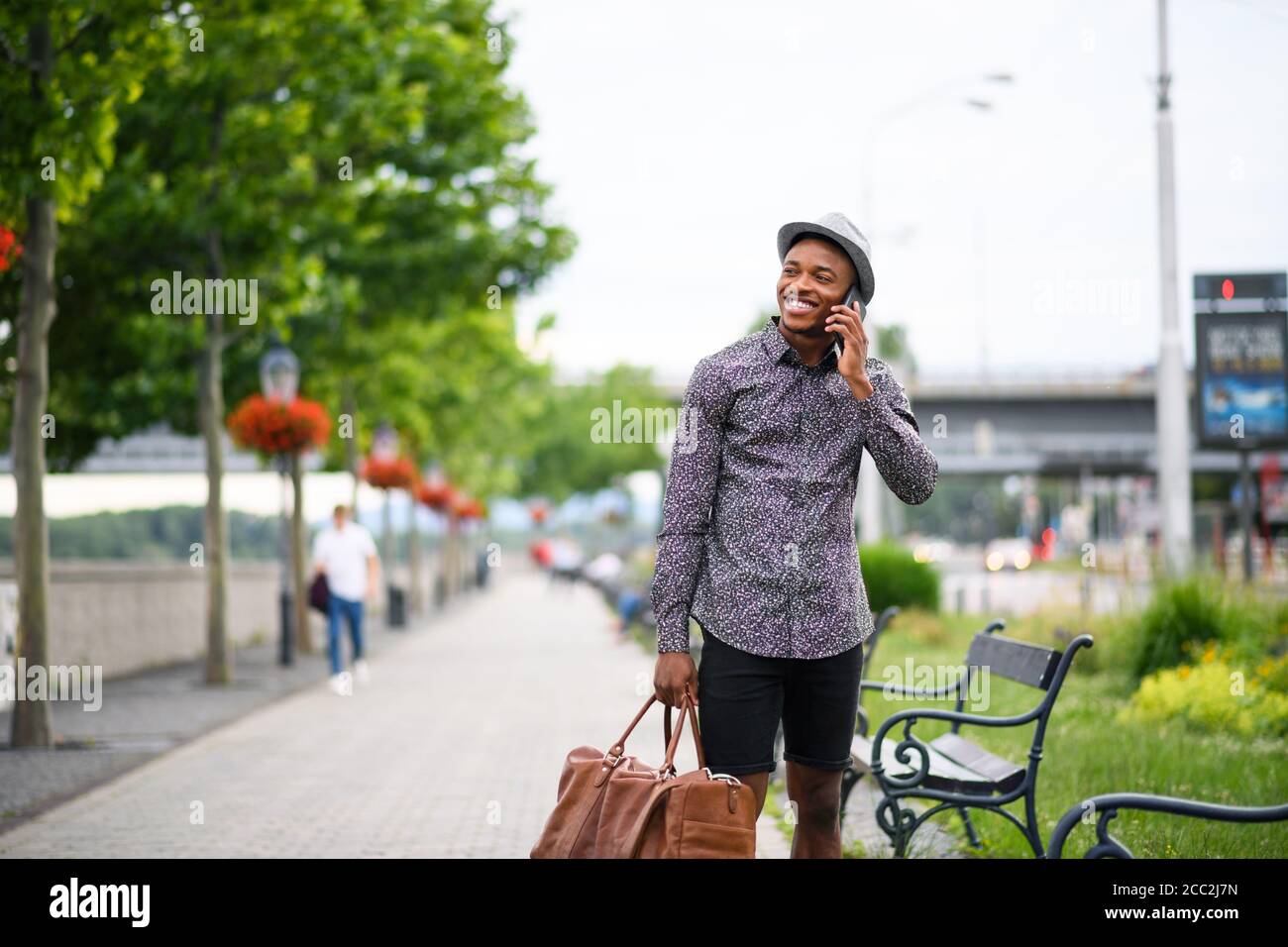 Cheerful young black man commuter outdoors in city, using smartphone. Stock Photo