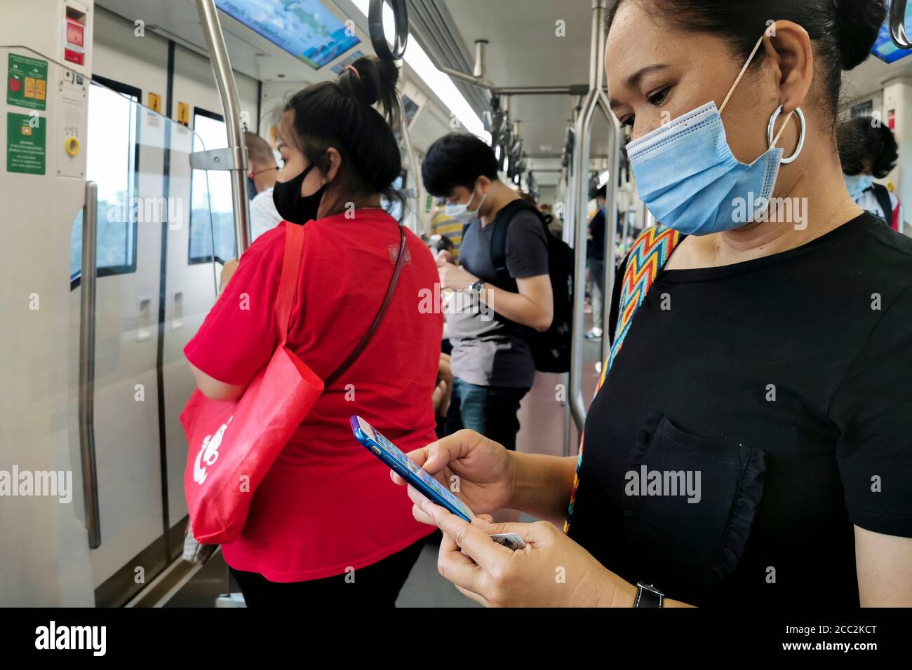Bangkok, Thailand - August 2, 2020 : asian passengers in sky train public transport wearing hygiene face mask going to work and checking pandemic news Stock Photo