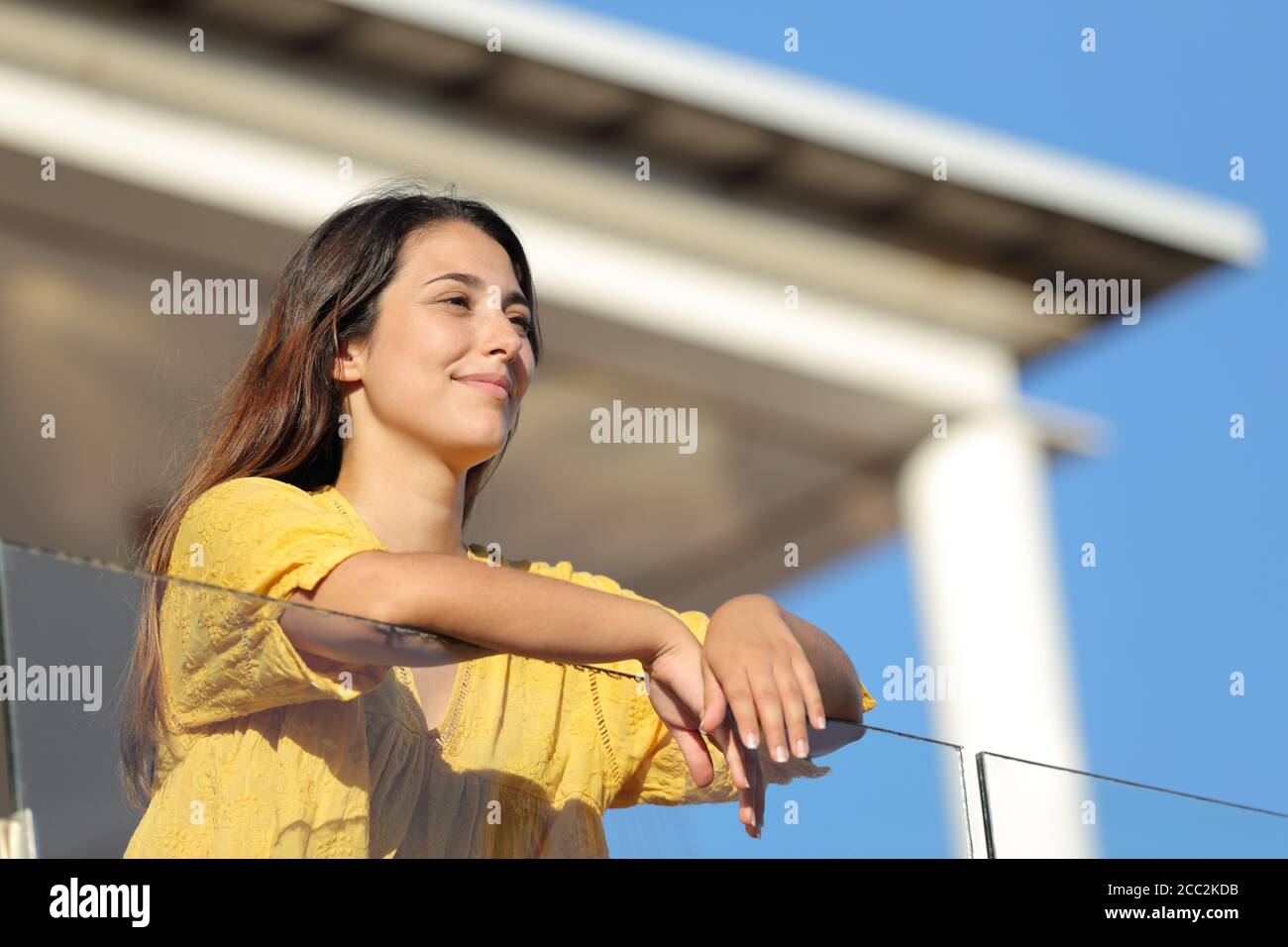Satisfied woman in yellow contemplating views in a balcony on summer Stock Photo