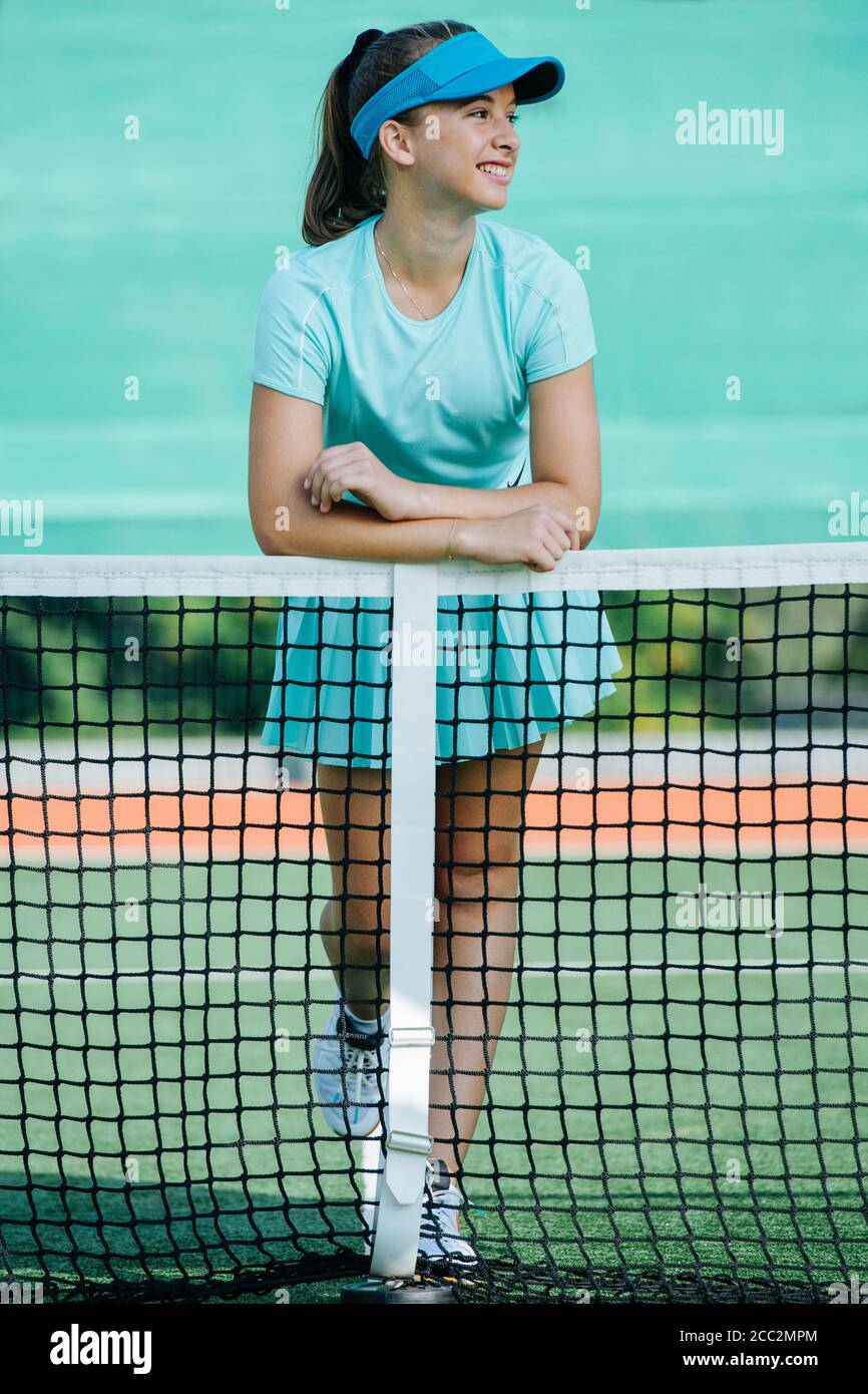 Young girl standing on tennis court, leaning on the net, grinning Stock Photo