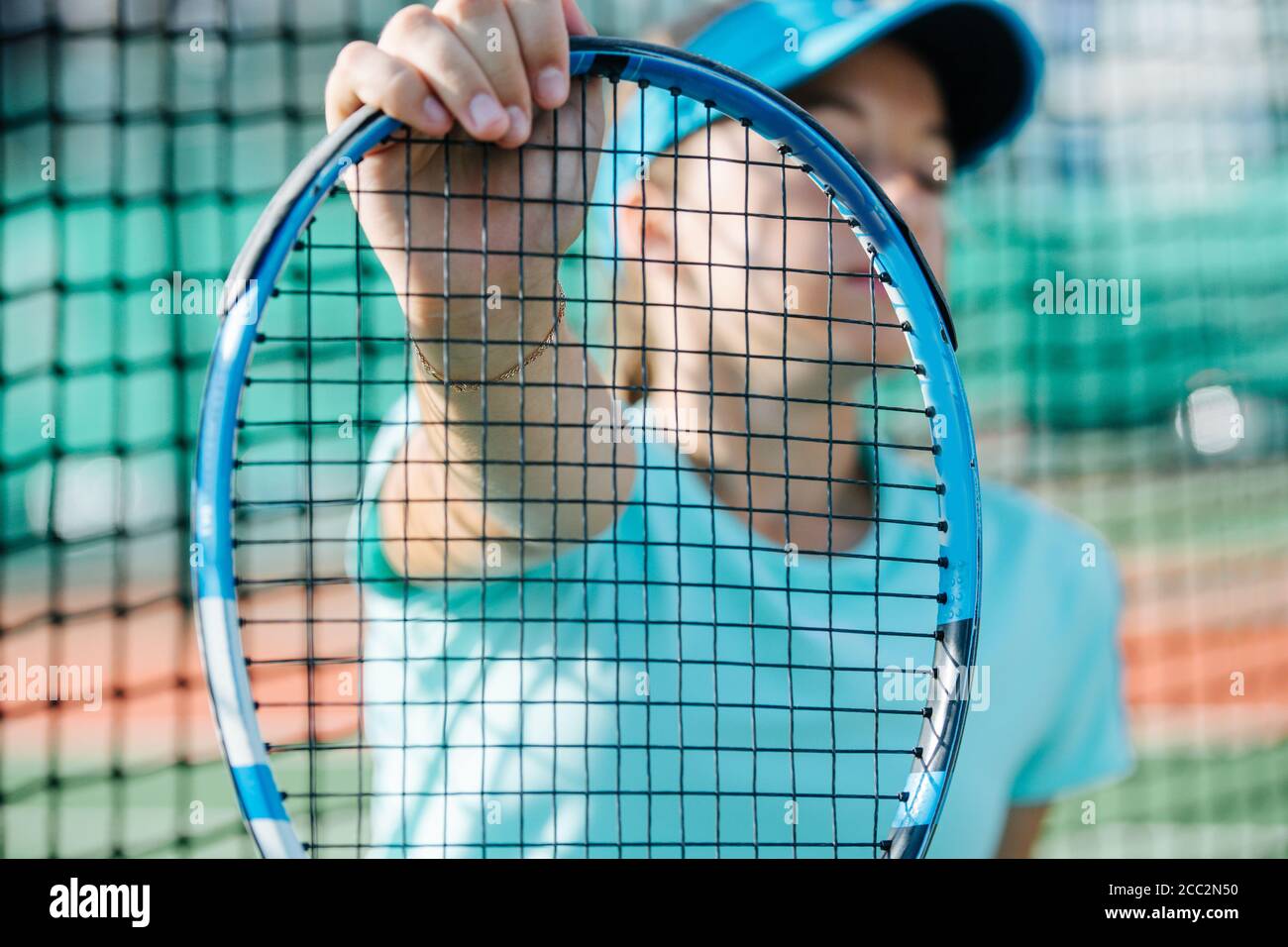 Teenage girl sitting on a tennis court, holding racket net close to camera Stock Photo