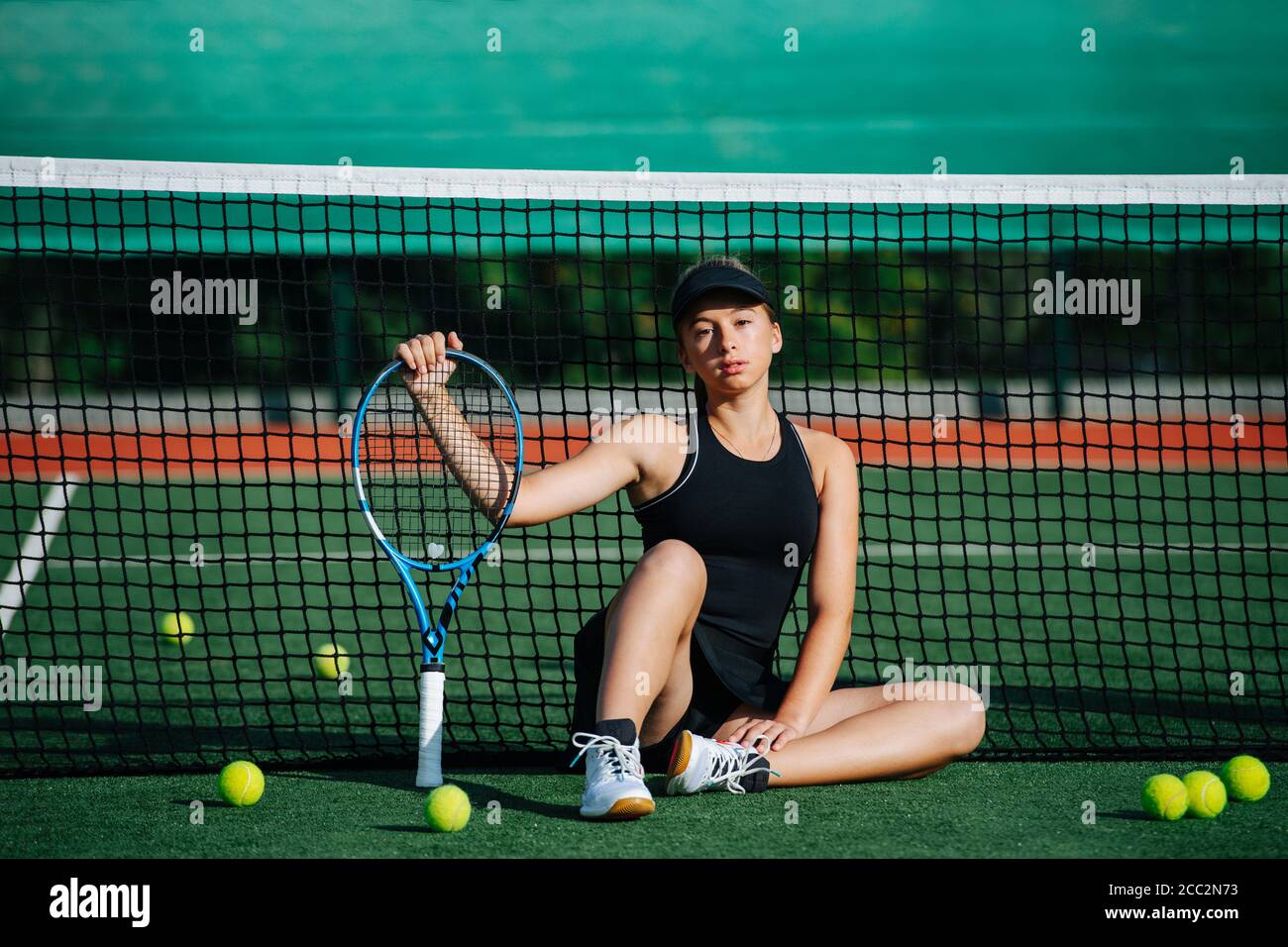 Portrait of a teenage girl sitting on a carpet tennis court, leaning on the net. Stock Photo