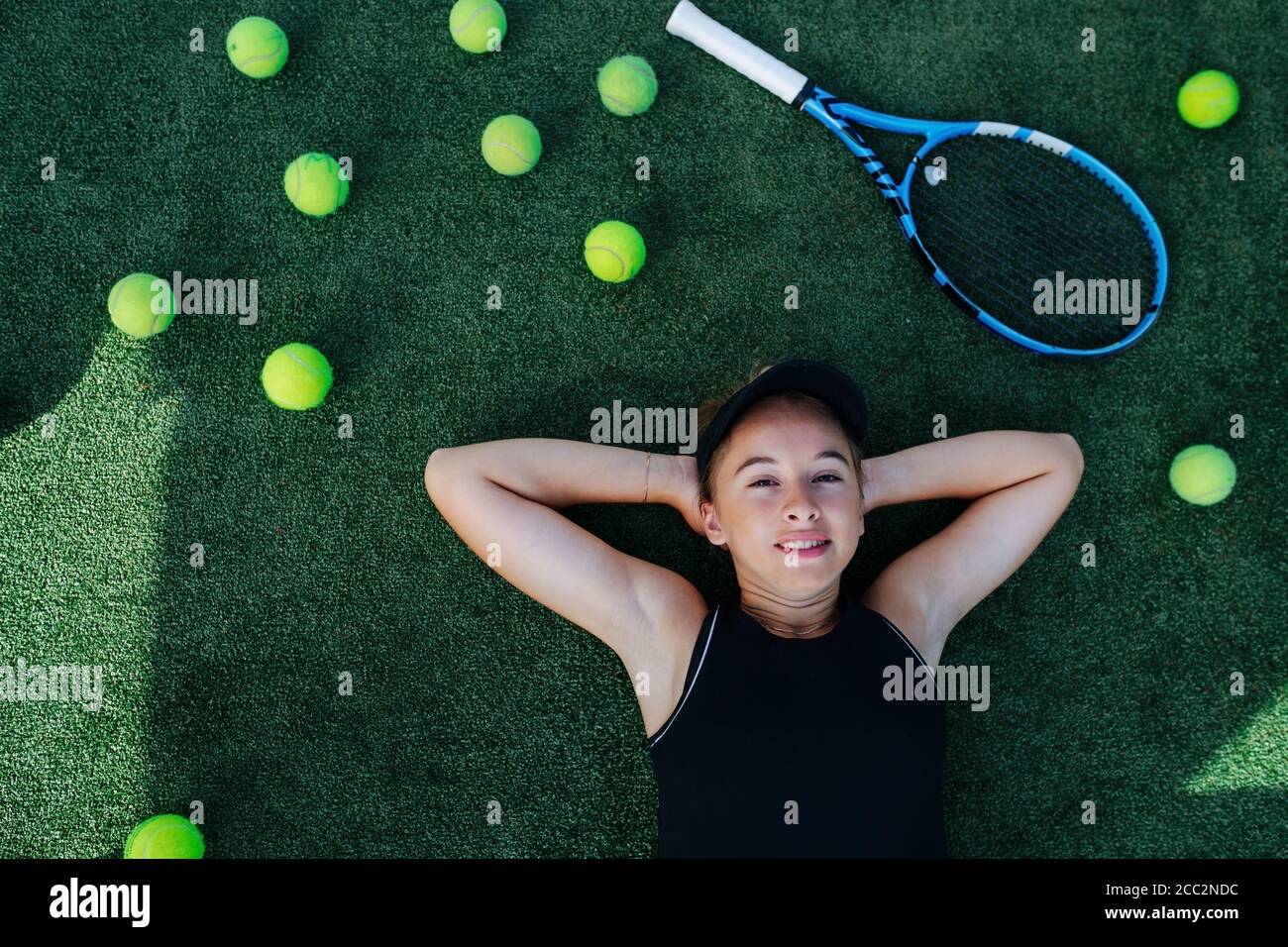 Relaxing teenage girl lying on her back on tennis court, looking at the camera Stock Photo