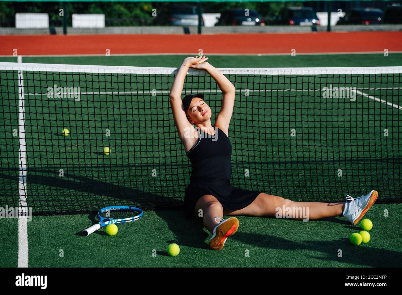Stretching teenage girl sitting on a tennis court, eyes closed. Stock Photo