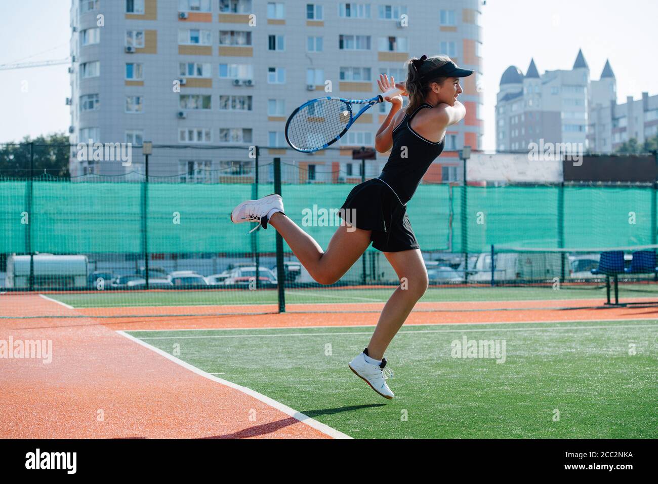 Young girl playing tennis on a new court, jumping while striking ball Stock Photo