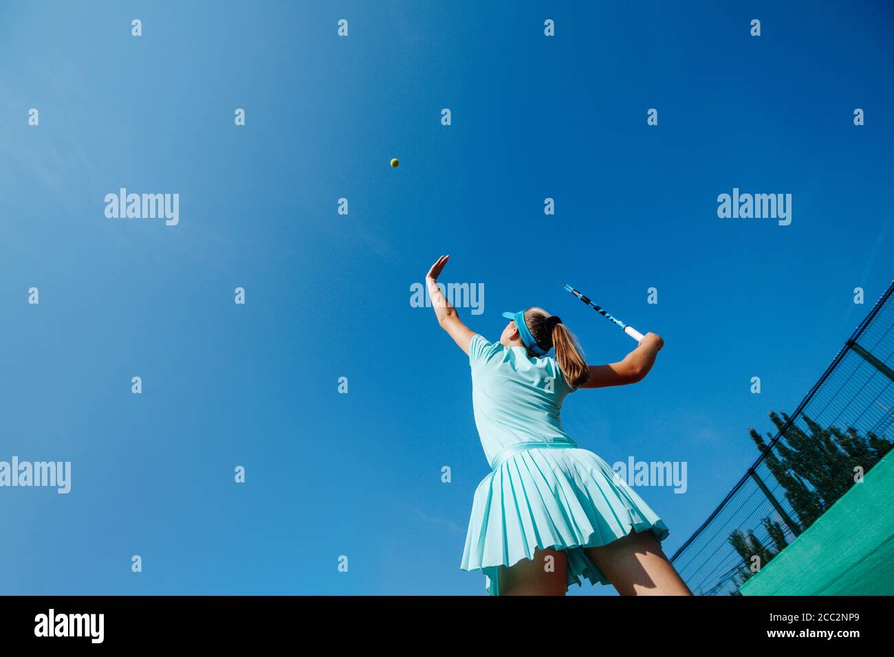 Low angle shot of a teenage girl playing tennis, throwing ball up and serving Stock Photo