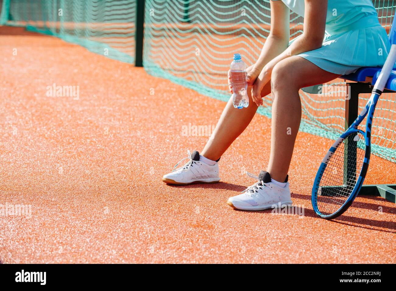 Legs of a girl sitting on a chair bench next to tennis court to take short break Stock Photo