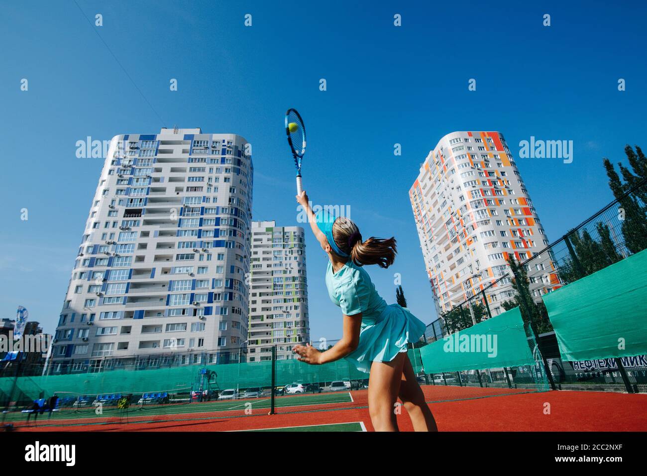 Eager girl training on a new tennis court, throwing ball up and serving Stock Photo