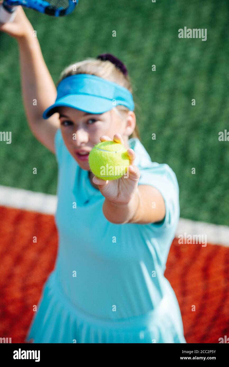 Focused girl training on a new tennis court, throwing ball up and serving Stock Photo