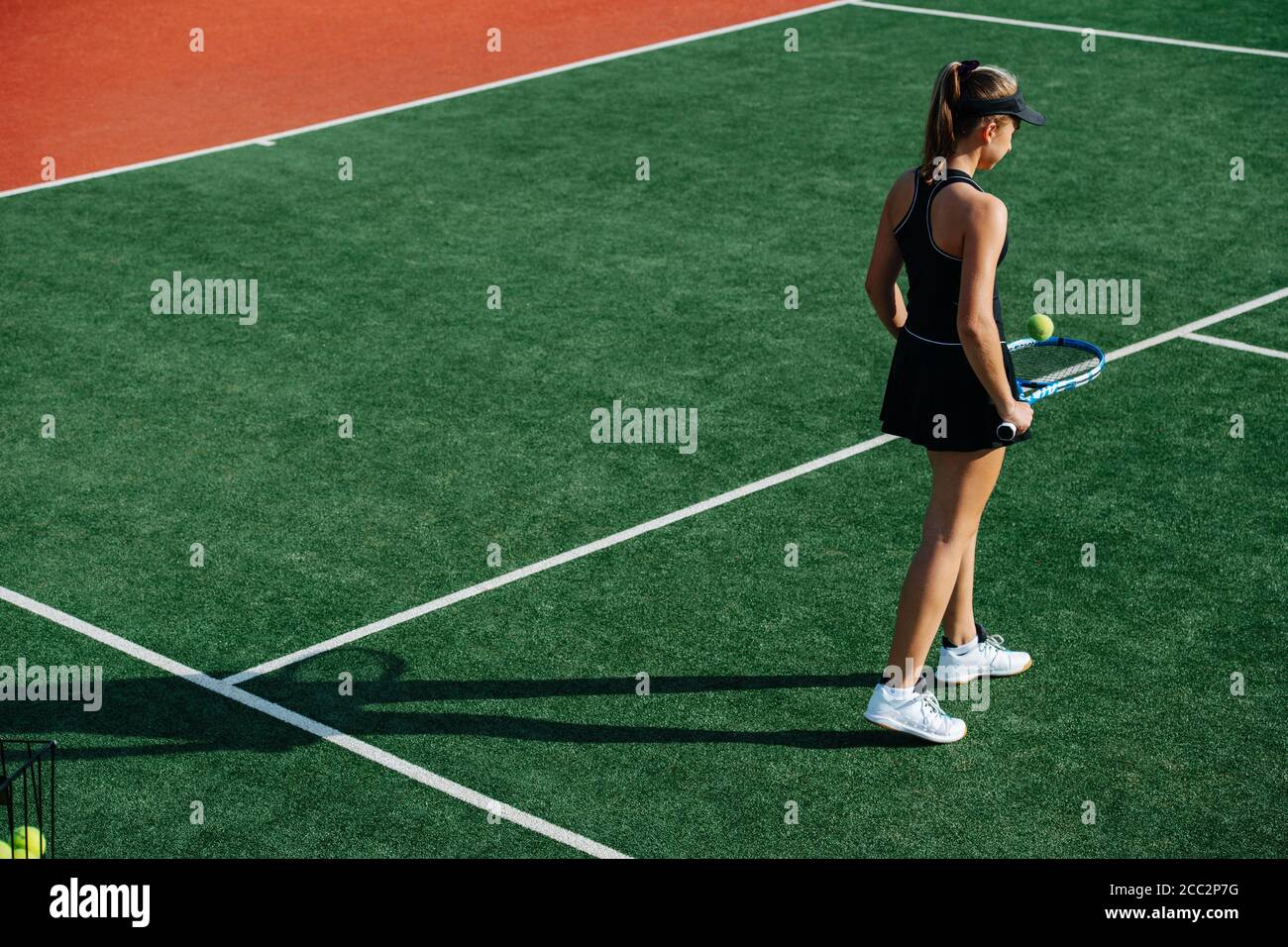 Slim teenage girl walking on a new tennis court, bouncing ball off her racket Stock Photo