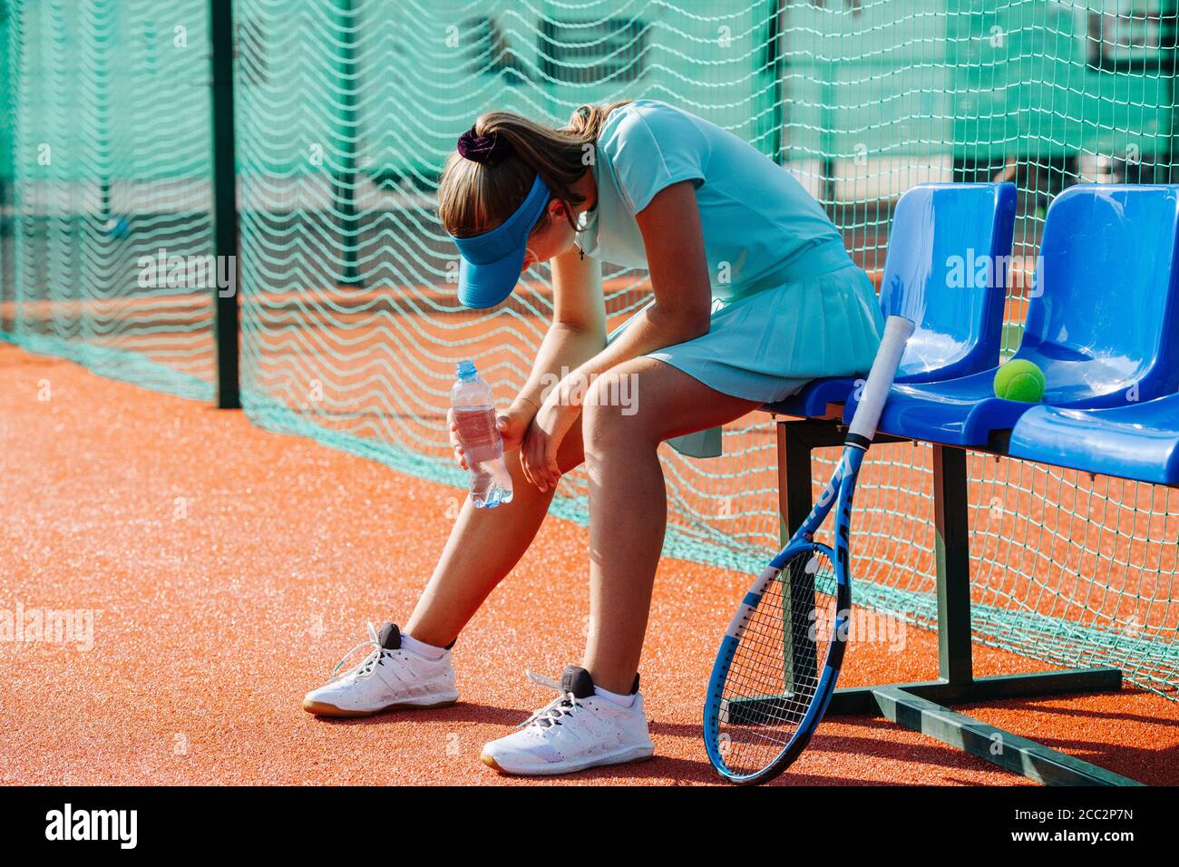 Tired girl sitting on a chair bench next to tennis court to take a short break Stock Photo