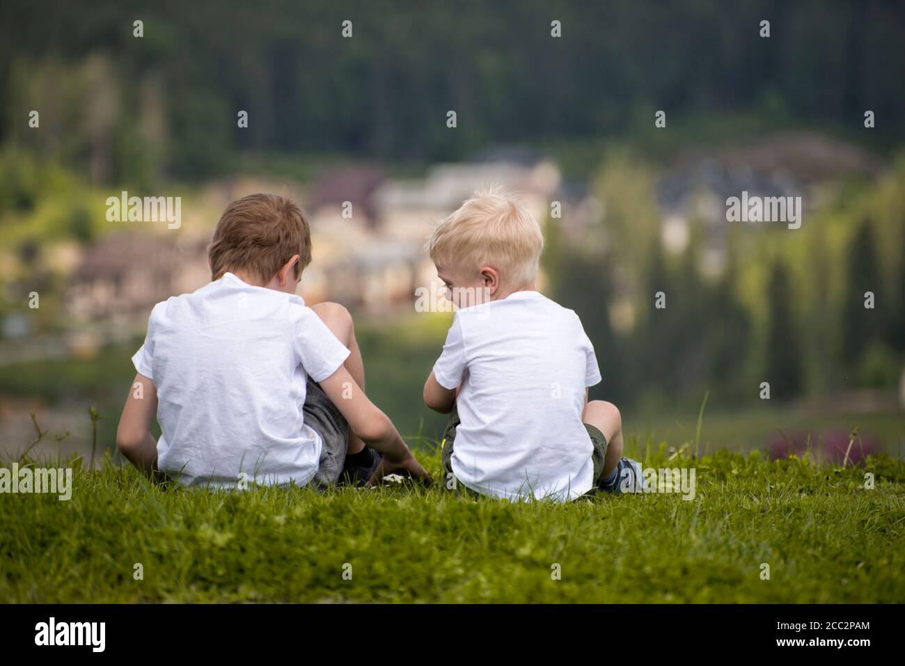 Two boys sit on a hill and have fun. Back view Stock Photo - Alamy