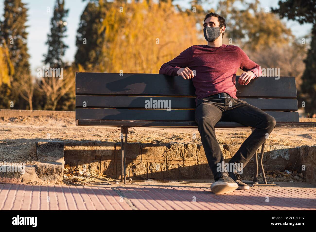 Shot of a male with a mask sitting on the bench in a park - the new ...