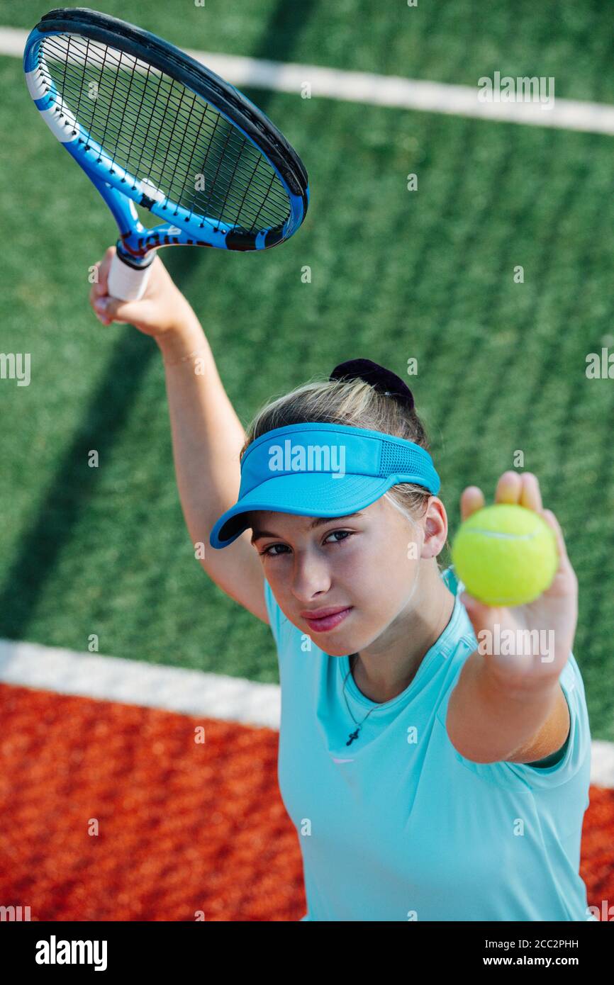 Hard working girl training on a new tennis court, throwing ball up and serving Stock Photo