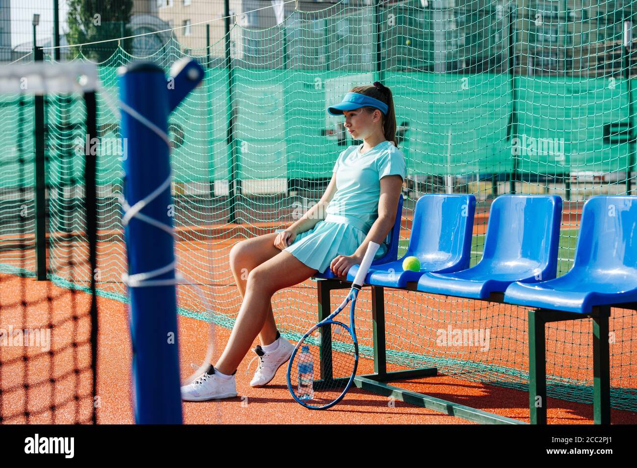 Emotionless girl sitting on a chair bench next to tennis court Stock Photo
