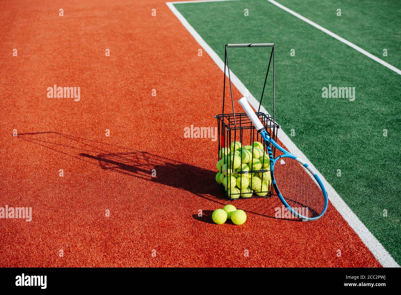 Ball basket and a racket lying next to green inner tennis court zone