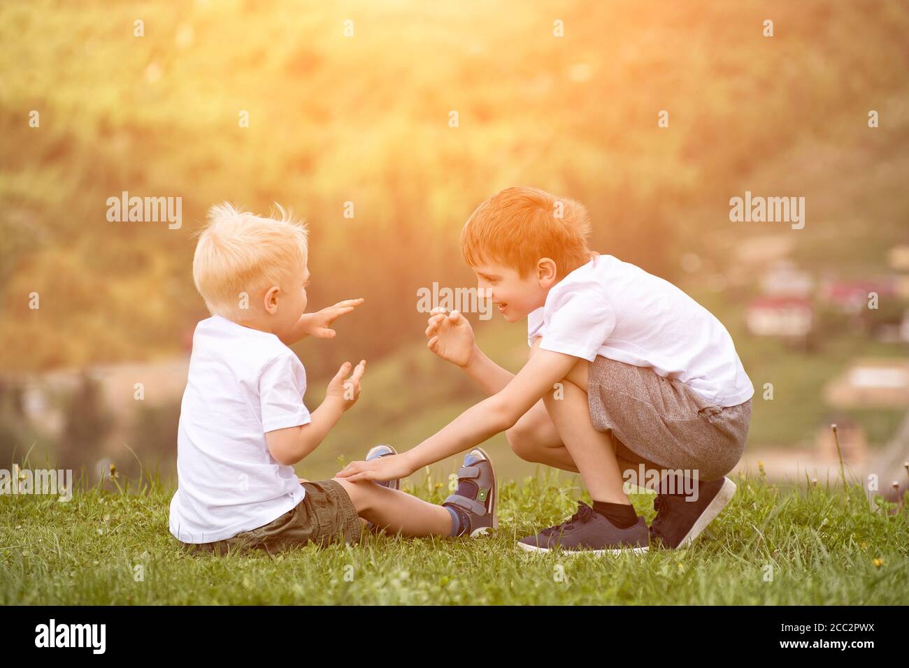 Two boys sit on a hill and have fun. Back view Stock Photo - Alamy