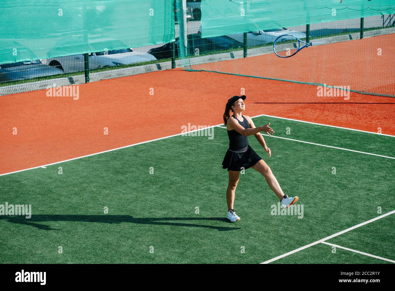 Carefree girl training on a tennis court, playing with racket, throwing it up Stock Photo