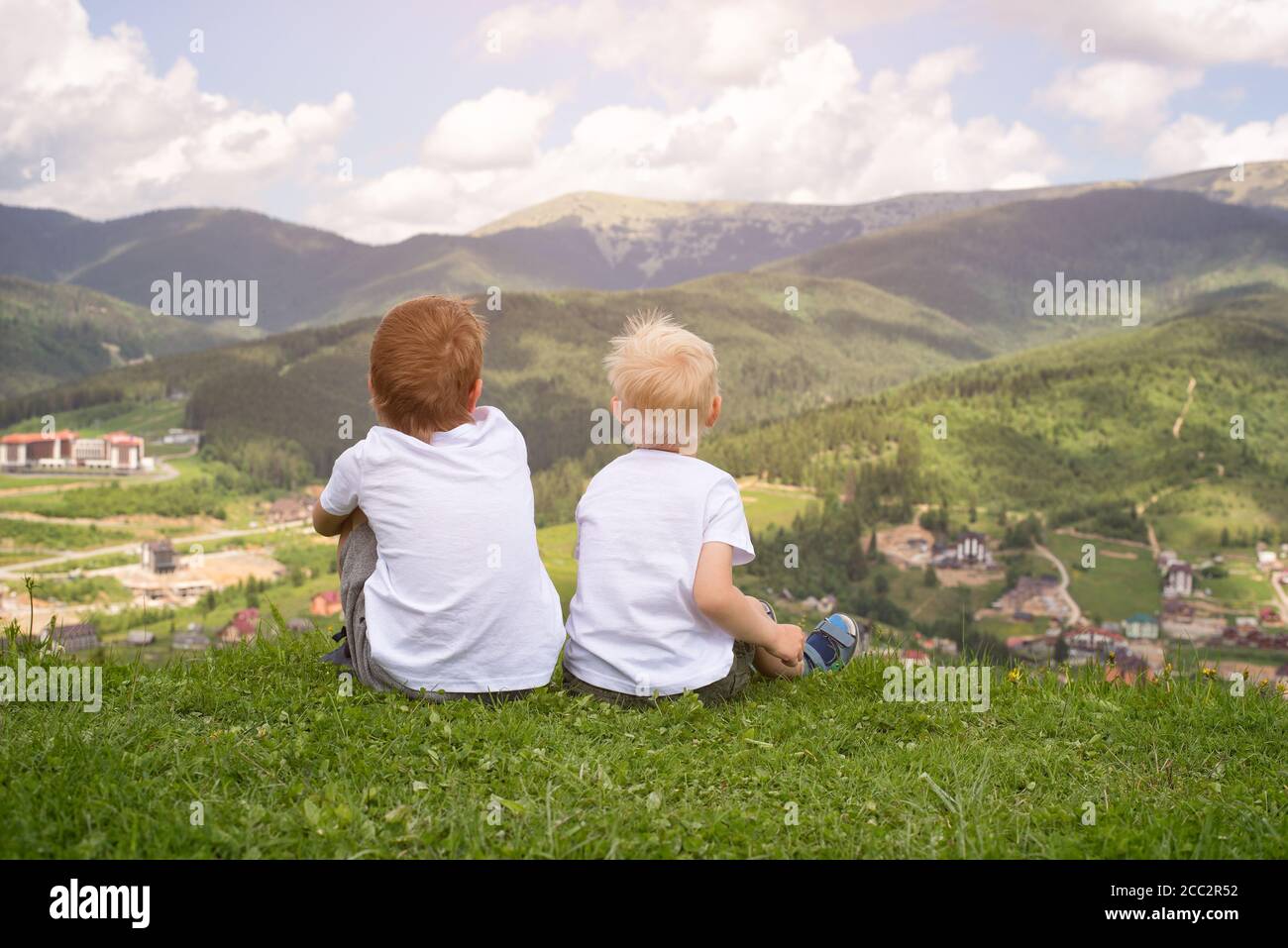 Two boys sitting on a hill and looking at the mountains. Back view ...