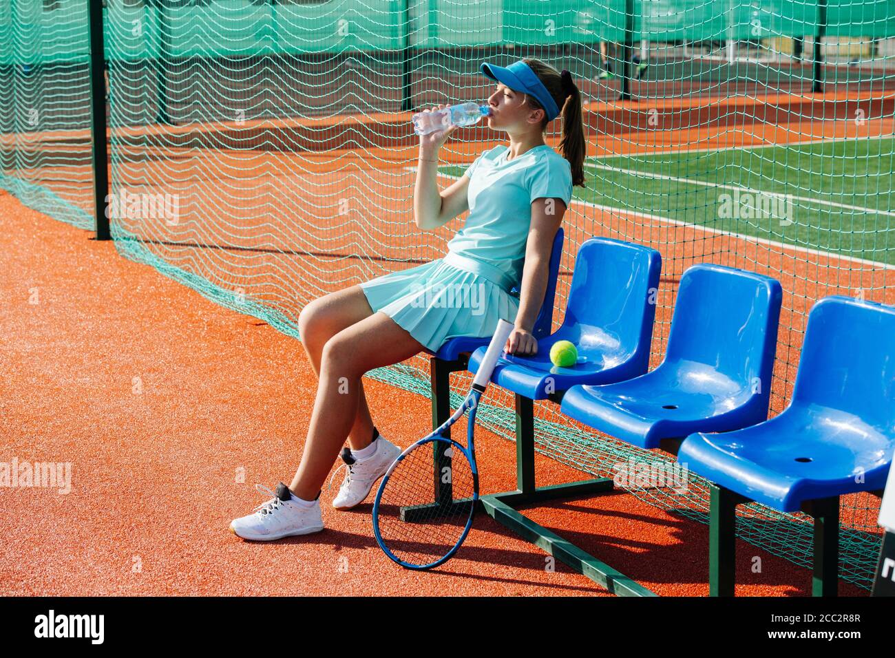 Teenage girl sitting on a chair bench next to tennis court to take a short break Stock Photo