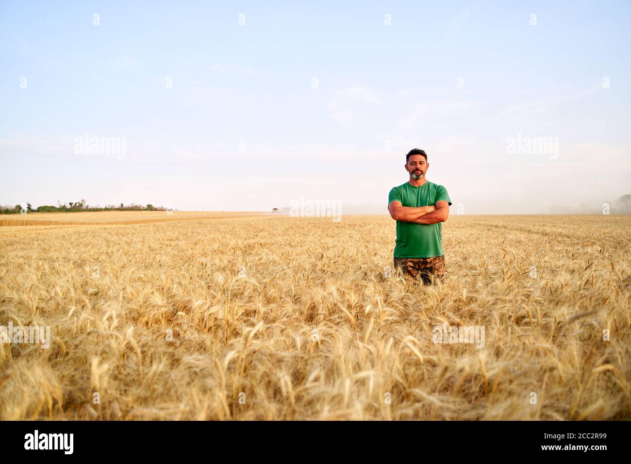 Happy farmer proudly standing in wheat field with arms crossed on chest ...