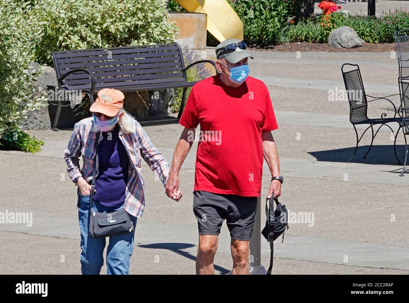 An elderly couple wearing facemasks walk through a shopping area along the Deschutes River in Bend, Oregon. Stock Photo