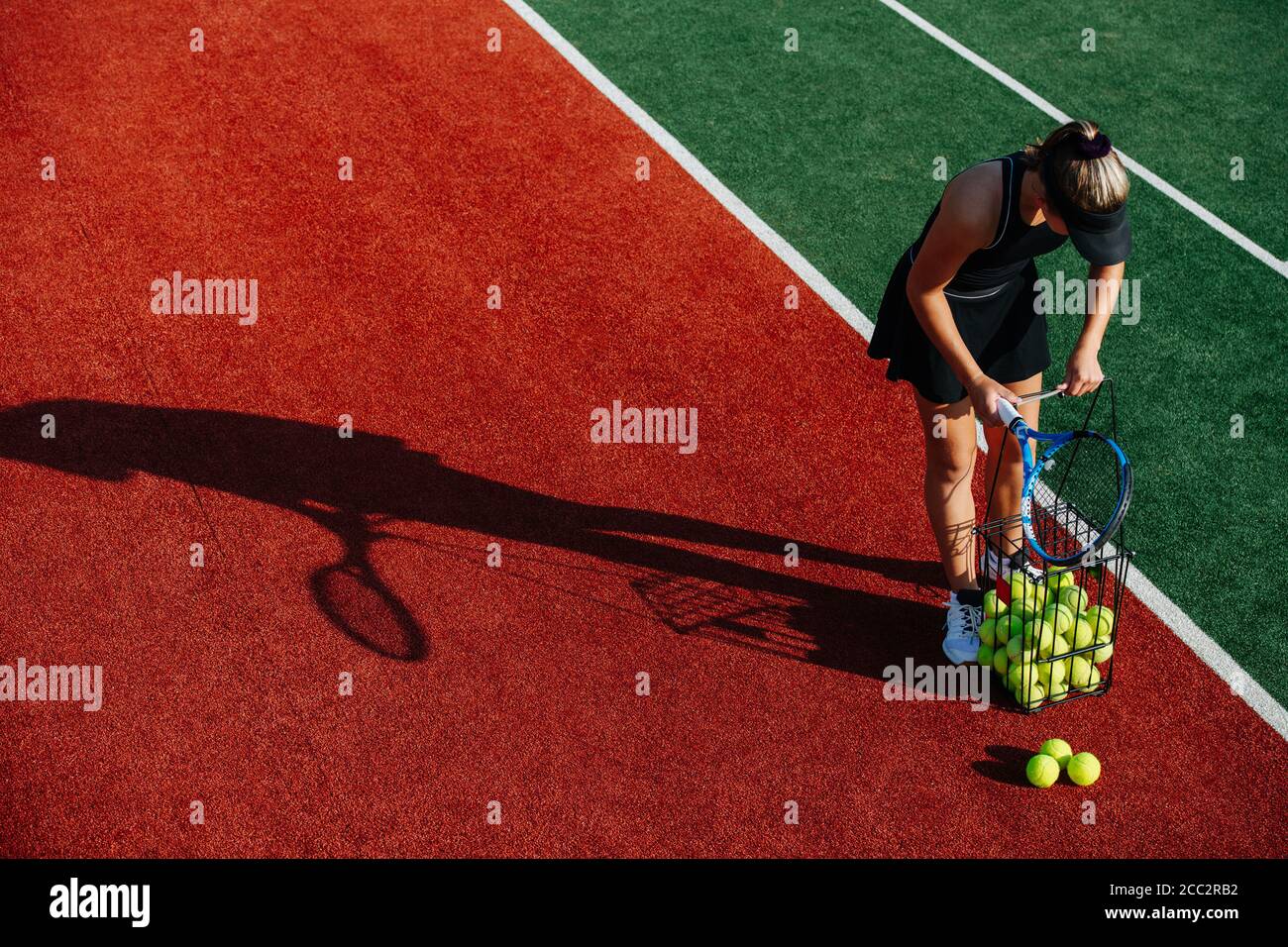 Young girl managing tennis ball basket on court. Stock Photo