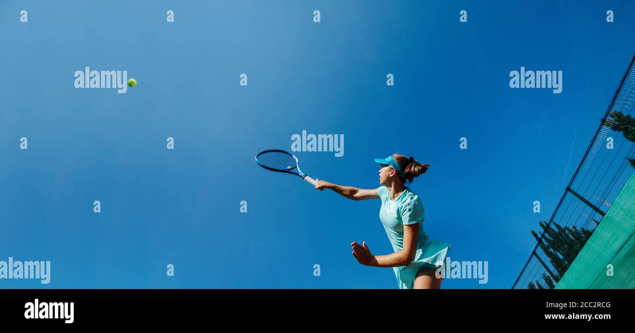Teenage girl playing tennis, striking ball high up with her racket Stock Photo