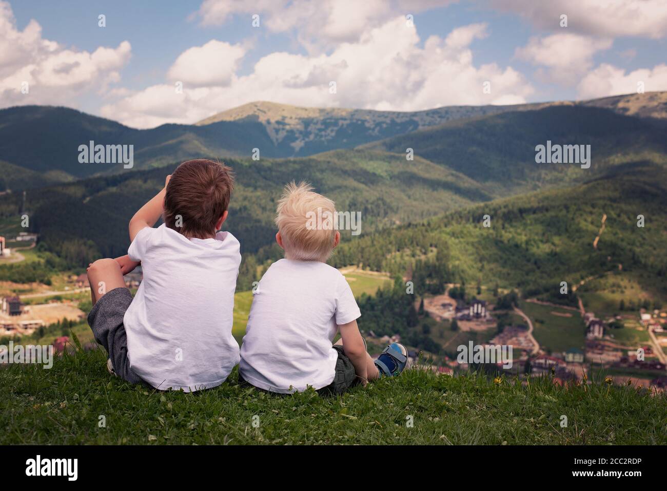 Two boys sitting on a hill and looking at the mountains. Back view ...
