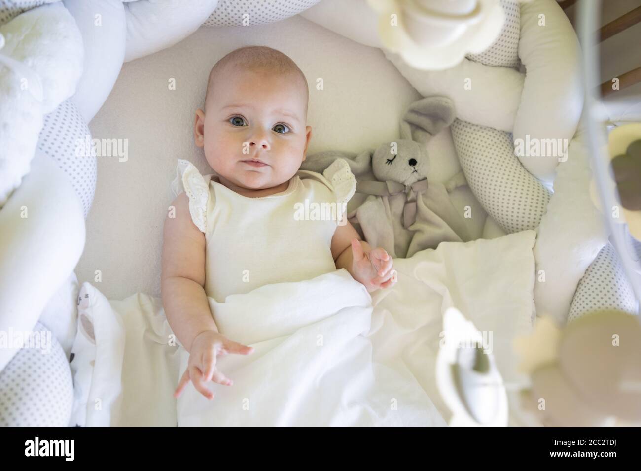 Adorable smiling baby girl with a toy bunny in cot Stock Photo