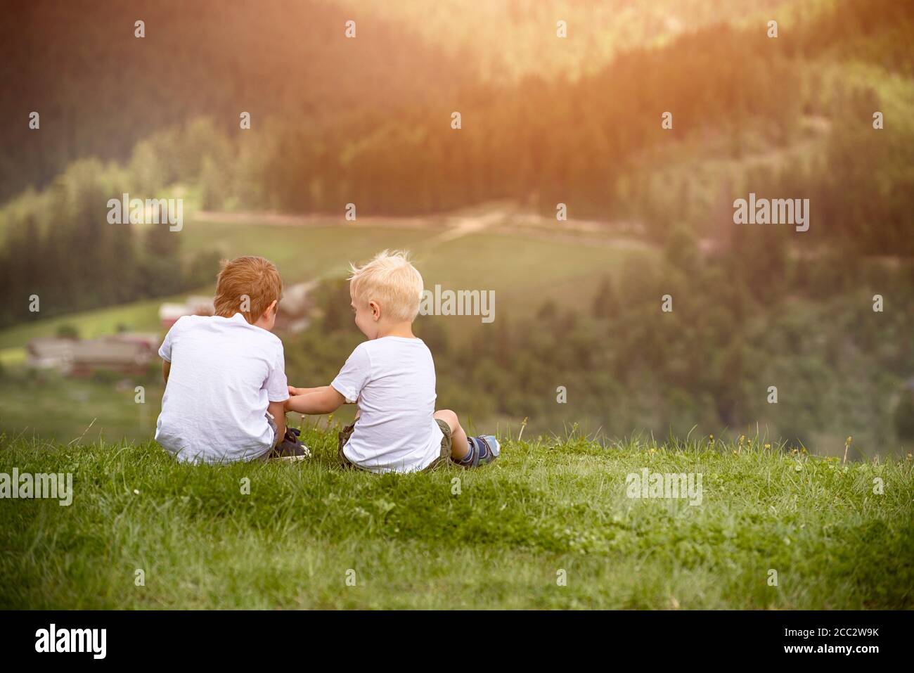 Two boys sit on the hill and talking cheerfully. Back view Stock Photo ...