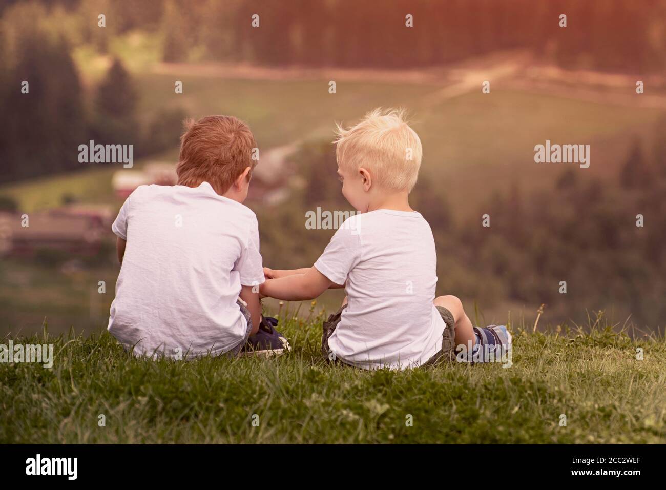 Two boys sit on the hill and talking cheerfully. Back view Stock Photo ...